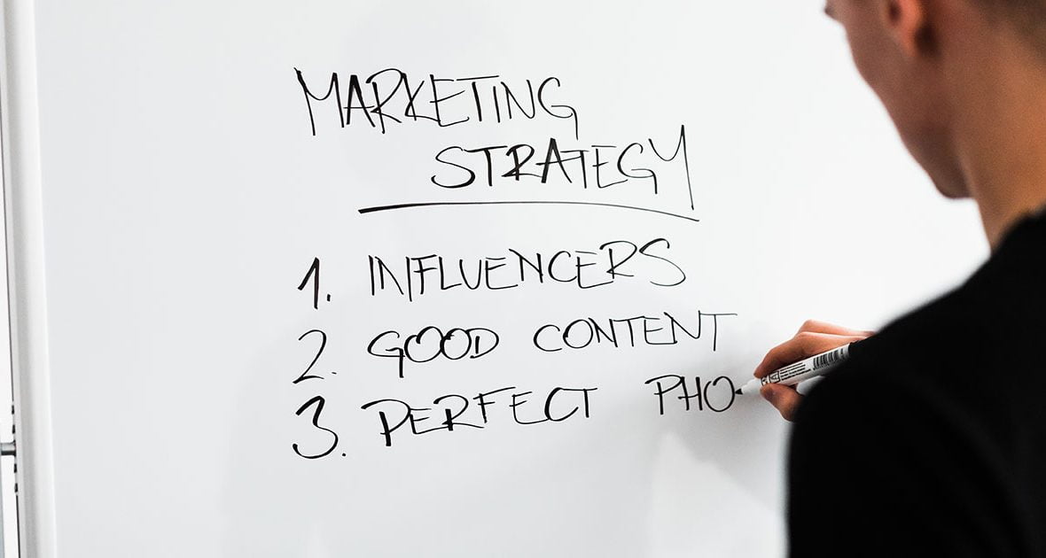 homem escreve marketing strategy num quadro branco